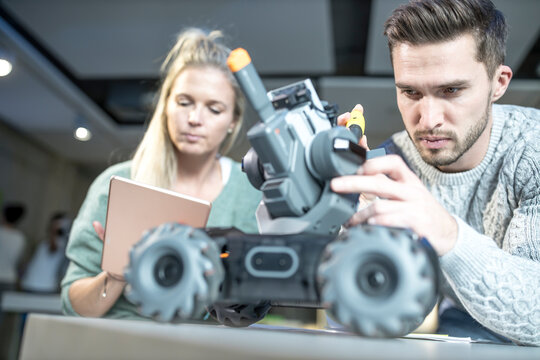 Engineer repairing combat car with colleague programming at workshop