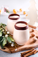 Winter eggnog cocktail in glass with chocolate rim on wooden board