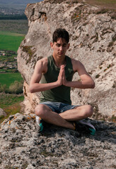 Sports man practices yoga on the top of the mountain. Meditation and exercise in nature.