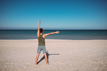 Young man practices yoga on the beach near the blue ocean. Meditation and exercise of an athletic guy.