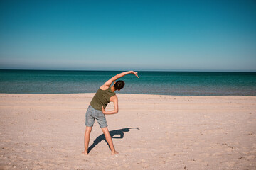 Young man practices yoga on the beach near the blue ocean. Meditation and exercise of an athletic guy.