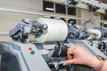 Cotton Yarn Production in a Textile Factory. Woman's hands worker in work. Row of automated machines for yarn manufacturing. Modern Textile Plant.Selective focus.