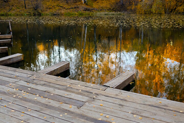 Wooden pier by the lake. Reflection of the autumn forest in the water. No people