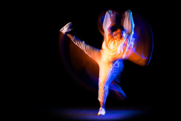 Sportive young girl in white costume dancing hip-hop dance isolated on dark background at dance hall in neon mixed light.