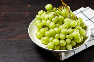 Branch of ripe green grape on plate with water drops. Juicy grapes on wooden background, closeup. Grapes on dark kitchen table with copy space