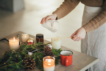 Woman making candle of soy wax, using wooden stick.