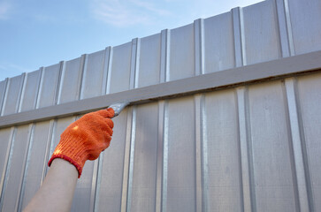 Painting the fence. Woman's hand painting steel fence with a brush