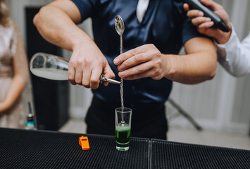 Man, bartender pours cocktail into shot glass.
