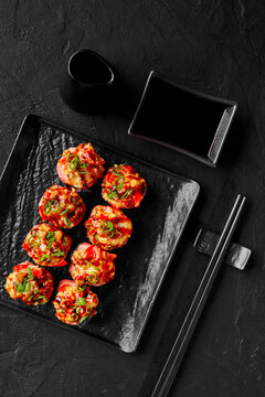 Sushi rolls in mamenori with chopped shrimp, tomato, scallions served with soy sauce on black background