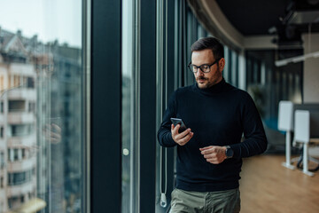 Focused adult man with glasses, checking his phone for e-mails from his superior.