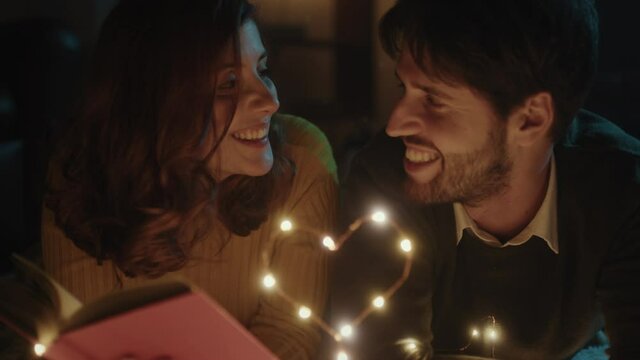 Ragazzo e ragazza su tappeto bianco per San Valentino con cuore in filo di luci led legge libro