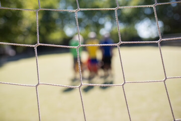 Close-up of football net on summer day. Blurry senior men standing on field in background. Football, sport, leisure concept