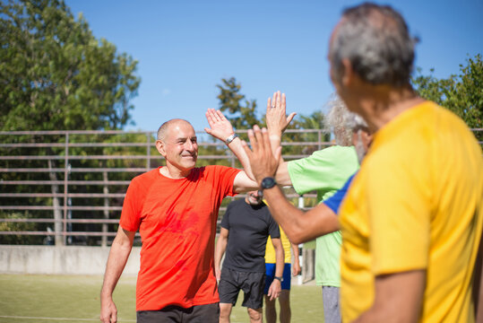 Energetic senior thanking each other after match. Men with grey hair in sport clothes standing in row on sport field, giving high fives. Football, sport, leisure concept - Powered by Adobe