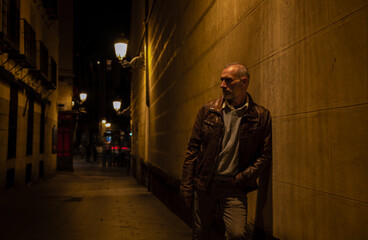 Adult man on street against brick wall with light of street lamp at night. Shot in Madrid, Spain