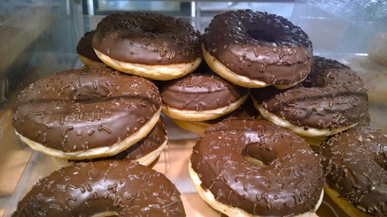 Donuts with black chocolate glaze supermarket shelves for sale. Sweet doughnut. Unhealthy Food with sugar. Bakery homemade product made from scratch. Close-up cake. Fashionable food trends. Freshness.