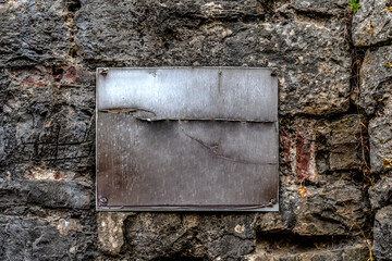 A metal rusty scratched blank plaque screwed with four screws to a stone wall. Vintage rough background with copy space. Real template