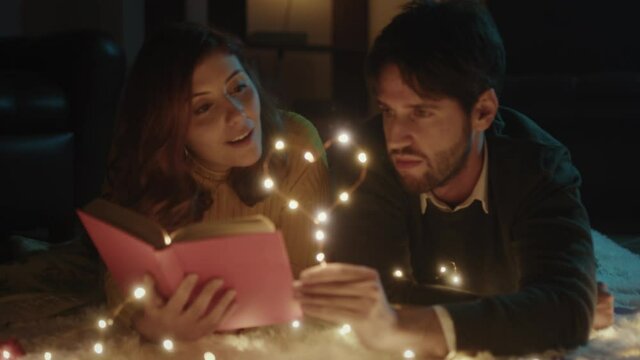 Ragazzo e ragazza su tappeto bianco per San Valentino con cuore in filo di luci led legge libro