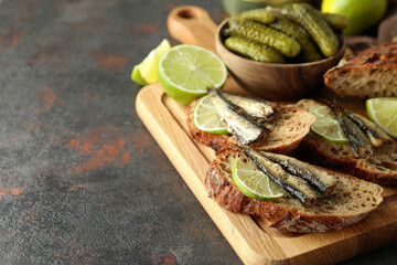 Board with sandwiches with sprats on textured background