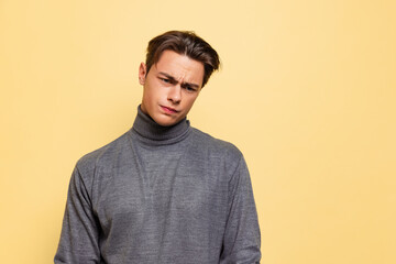 Studio shot of young handsome displeased man, student wearing warm gray polo-neck isolated on...
