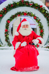 Santa Claus posing with a bag of gifts on the background of Christmas decorations outdoors