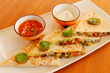 mexican food quesadilla, spicy cooked chicken and vegetable stuffed in tortilla bread with cheese, guacamole, tomato salsa and sour cream
