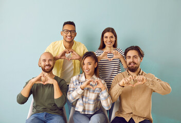 Group portrait of happy thankful young diverse multiracial multiethnic people smiling and doing heart shape hand gesture against blue color studio background. Love, support and gratitude concepts