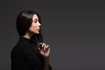 side view of young woman in black turtleneck holding scissors near long shiny hair isolated on dark...