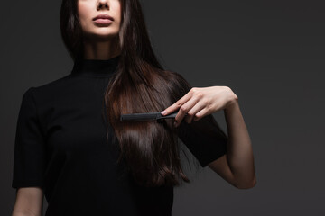 cropped view of young woman brushing long shiny hair with comb isolated on dark grey