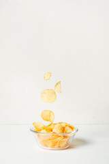 Potato chips falling into glass bowl on white background