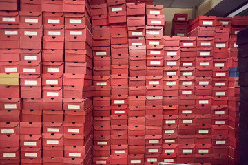 Big wall of lots of red cardboard package boxes with footwear stacked at a factory warehouse. Shoe...