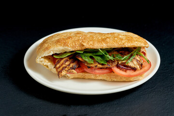 Ciabatta sandwich with pork steak and vegetables in white plate on black background
