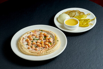 Hummus with olive oil, tahini and salted vegetables in a white plate on a black background