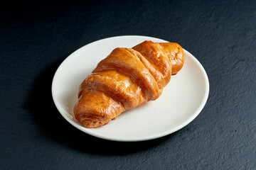 Creamy sweet croissant in white plate on black background