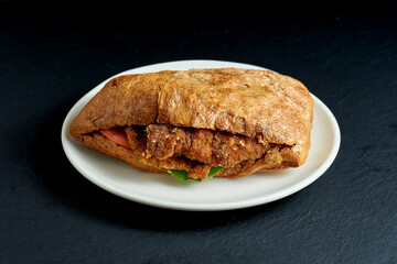 Ciabatta sandwich with tomatoes and schnitzel in a white plate on a black background