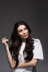 young dreamy woman with wavy hair looking away on dark grey