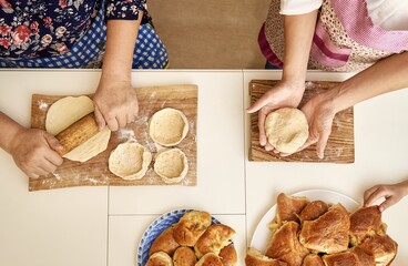 Senior woman with adult daughter kneads and rolls raw dough cooking delicious pies at white table in kitchen upper close view