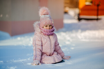 Child in pink knitted hat playing in snow on Christmas vacation. Winter outdoor fun. Little girl in knit scarf and mittens