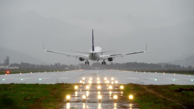 The plane approaches and lands early in the morning at the airport in the evening at sunset or dawn. Rear view. Against the background of mountains with snow-capped peaks. The runway lights lit up.