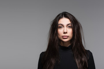 young woman in black turtleneck with tousled hair isolated on grey