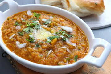 Indian Mumbai Street style Pav Bhaji, garnished with peas, raw onions, coriander, and Butter. Spicy thick curry made of out mixed vegetables served with pav over black background with copy space.