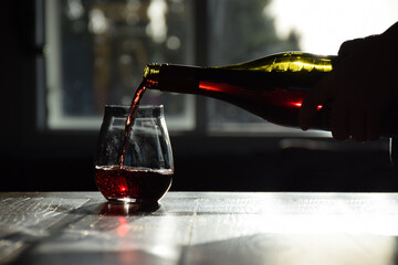 A fine red wine is poured into a stemless glass from a bottle
