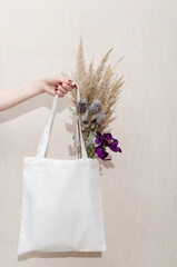 Mockup of a white tote reusable eco cotton shopper bag with dry grass and flowers on a white background. Eco friendly.
