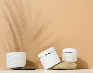 white round plastic jar for cosmetic products on a brown background. Palm leaf shadow. Blank for...