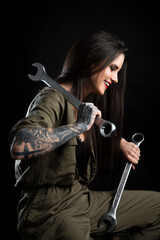 Atrakcyjna uśmiechnięta dziewczyna - mechanik z tatuażami, pozująca z dwoma bardzo dużymi kluczami. Zdjęcie studyjne na czarnym tle, oświetlenie z 2 lamp.