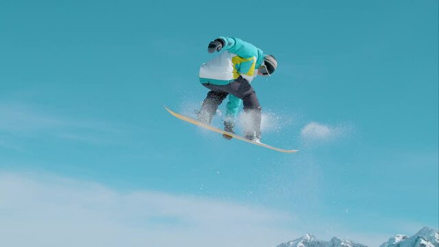 SLOW MOTION: Spectacular shot of a snowboarding pro doing a rotating grab stunt while training in Vogel ski resort snowpark. Male snowboarder soars through the air and does a breathtaking trick.