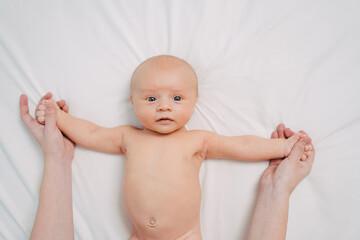 hands do exercises to baby on white sheet. gymnastics and massage for newborns.