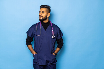 Indian surgeon standing setting his gloves to start the surgery, wearing a mask and a blue uniform, isolated on a blue background.