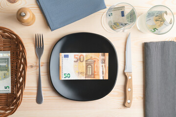 Conceptual studio shot of dinner table with euro bank notes on the plate instead of food. Concept for rising food prices, inflation, economic crisis, consumer prices index.