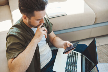 Caucasian man using mobile phone while sittingon the floor at home with laptop computer. Businessman using laptop. Business technology. Internet technology