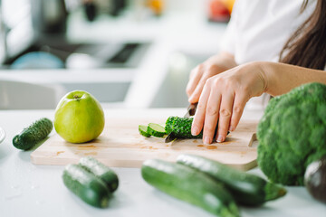 Woman preparing food in her kitchen. Female chopping fresh green vegetables on cutting board in light kitchen. Healthy eating, detox, diet.